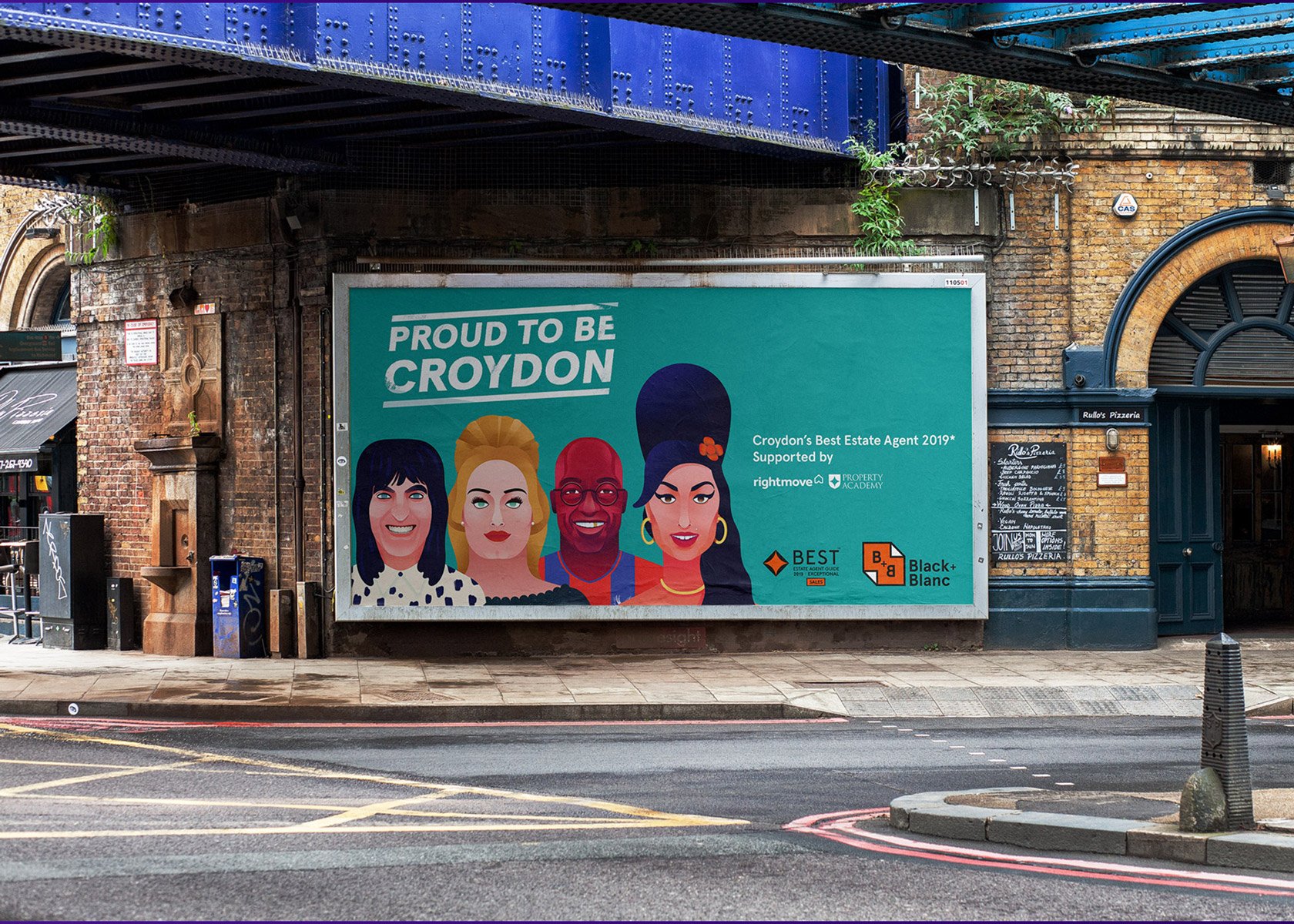 A hoarding under a railway bridge reads “Proud to be Croydon” with illustrated portraits of four diverse people. This sign, created by Growth by Design, promotes local estate agents and stands out on a quiet city street.