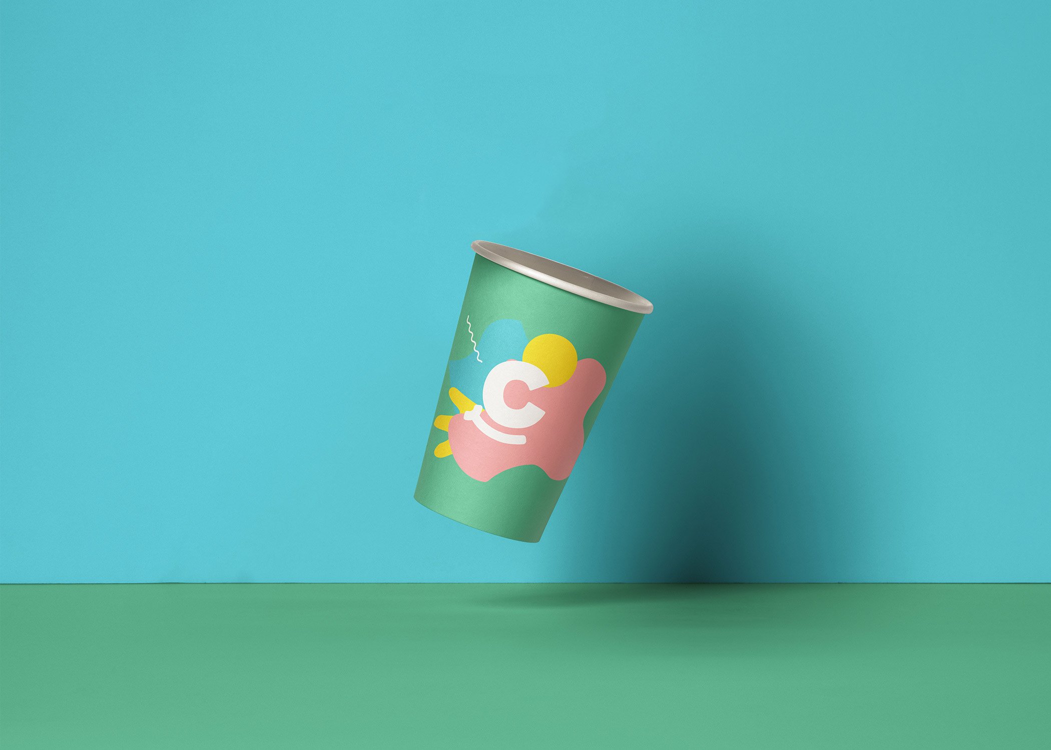 A colourful paper cup with abstract shapes and a letter "C" design floats above a green surface against a teal background, symbolising Growth by Design and scalable growth strategies for start-ups.