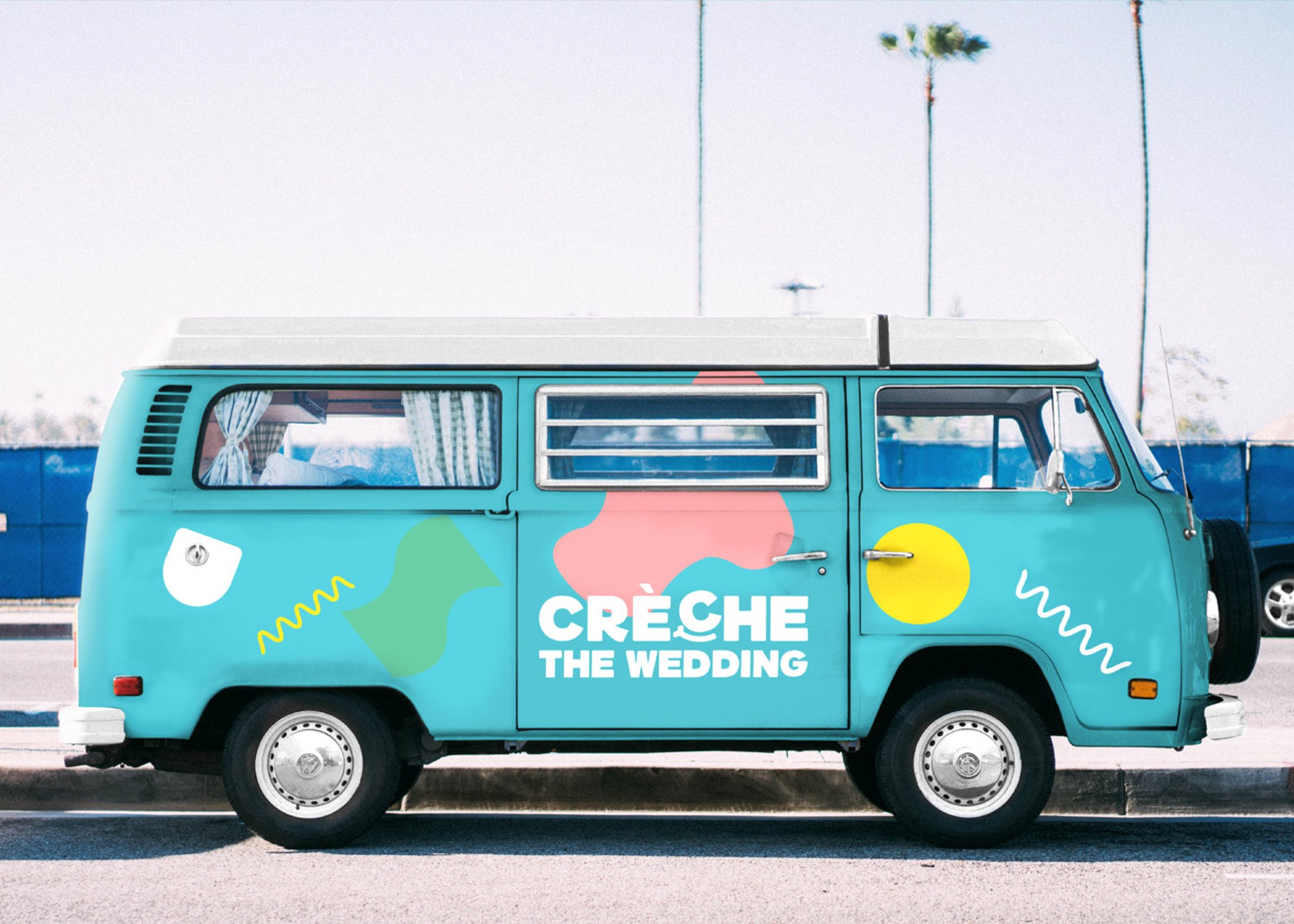 A turquoise van with colourful abstract shapes and the words "CRÈCHE THE WEDDING" on its side is parked by a street, reflecting the spirit of a strategically‑led branding studio. Two tall palm trees and a blue fence stand out under a clear sky.