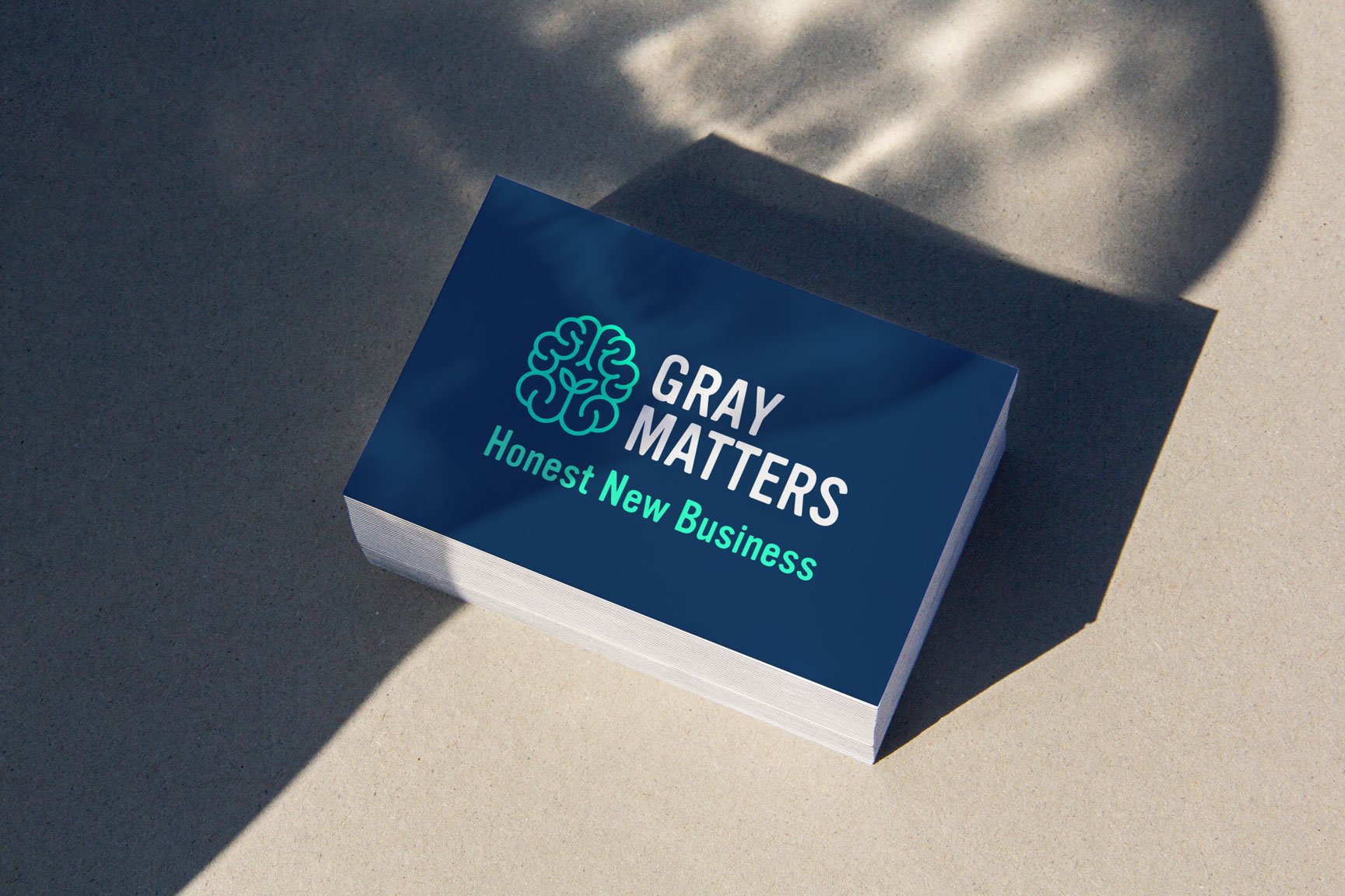 A stack of business cards on a light surface. The top card, by a strategically‑led branding studio, features a blue background, brain-shaped logo, and the text "GREY MATTERS" and "Honest New Business" in white and light green.
