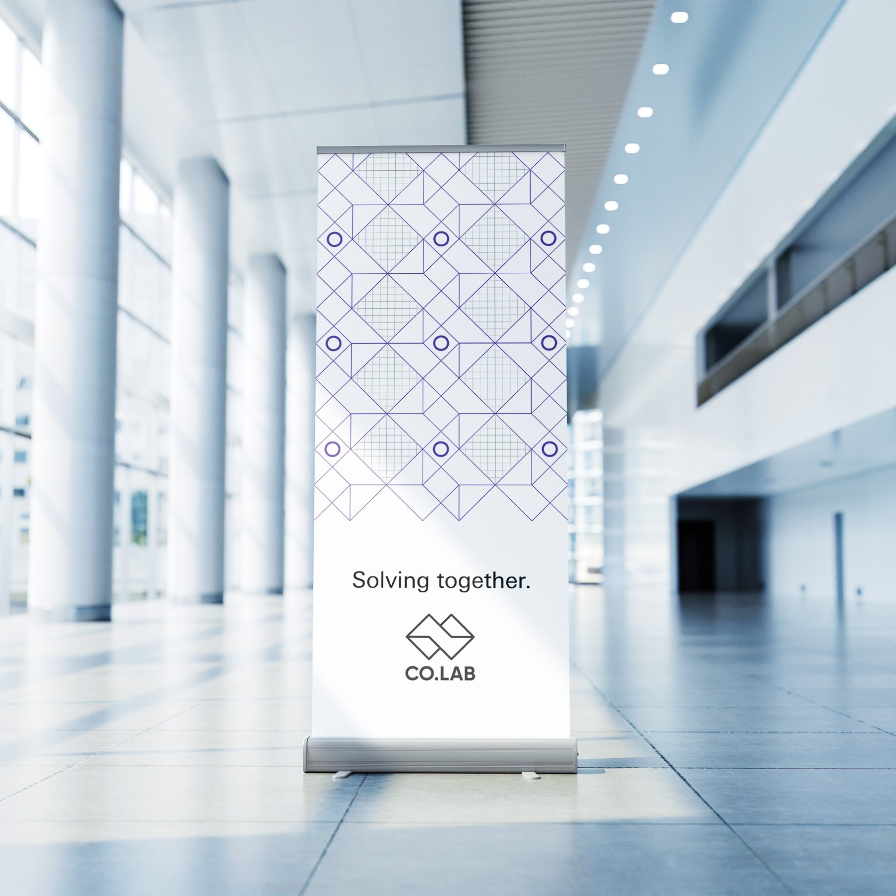 A standing banner in a bright, modern corridor displays a geometric pattern, the text “Solving together,” and the CO.LAB logo at the bottom—reflecting a strategically‑led branding studio focused on scalable growth strategies for start‑ups.