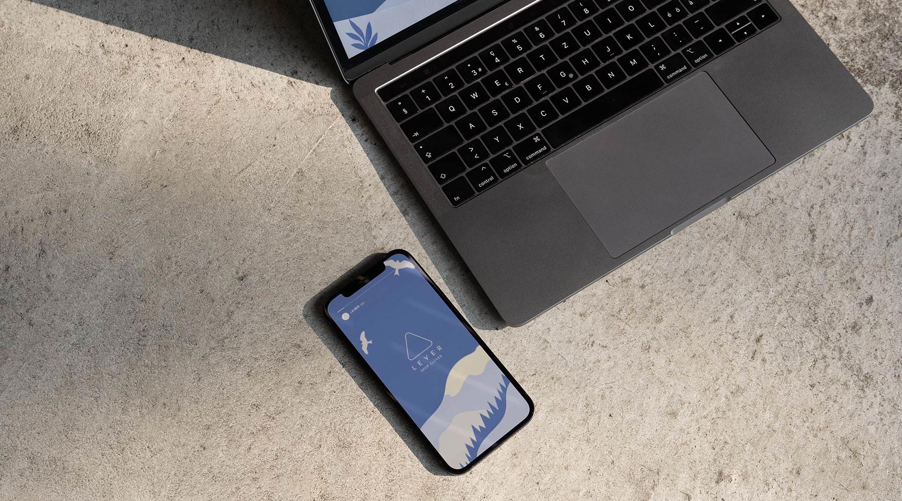A black laptop and a smartphone with a minimalist mountain landscape wallpaper rest on a textured, light-coloured concrete surface in natural sunlight—an inspiring setup for scalable growth strategies for start‑ups.