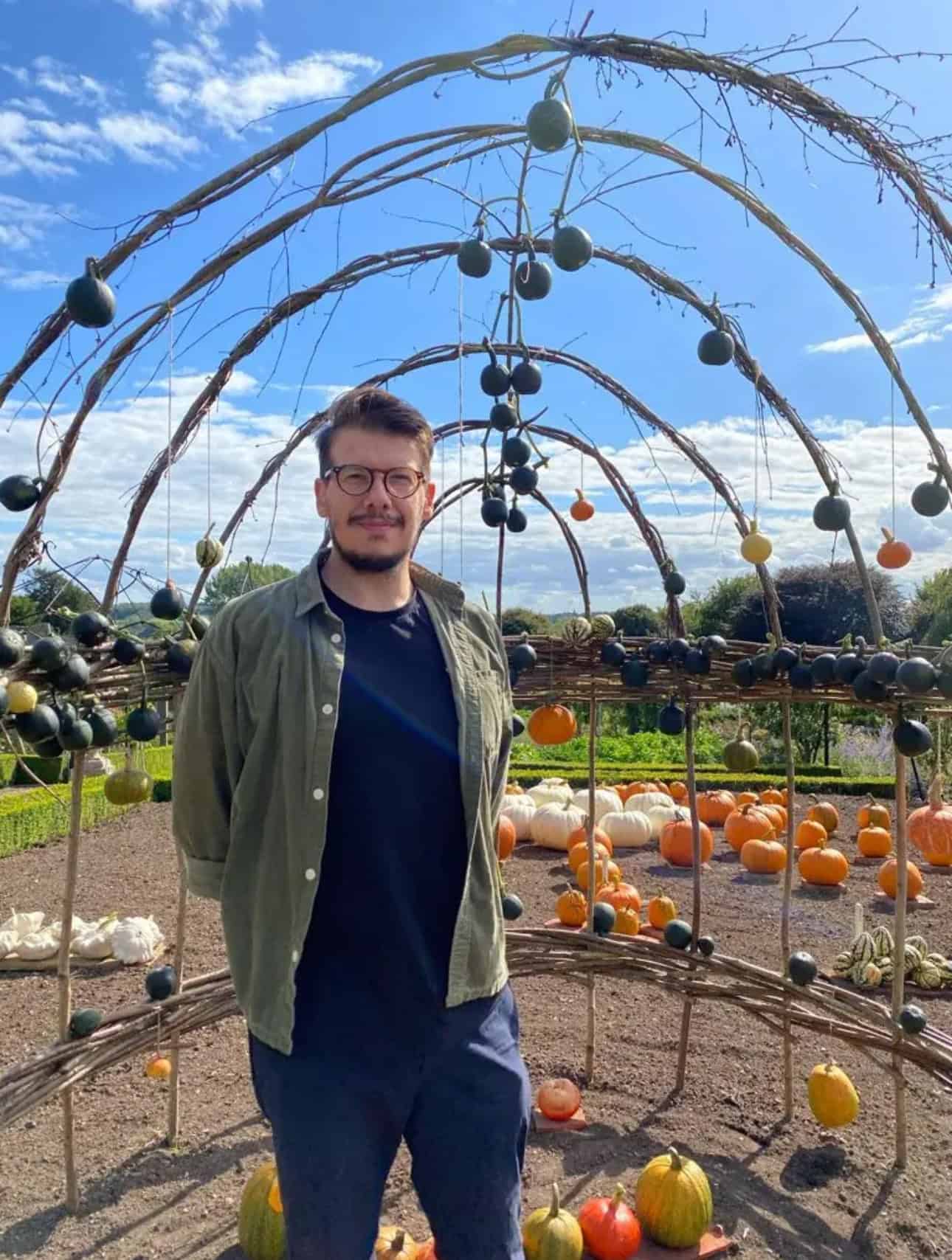 Person standing among various pumpkins and gourds.